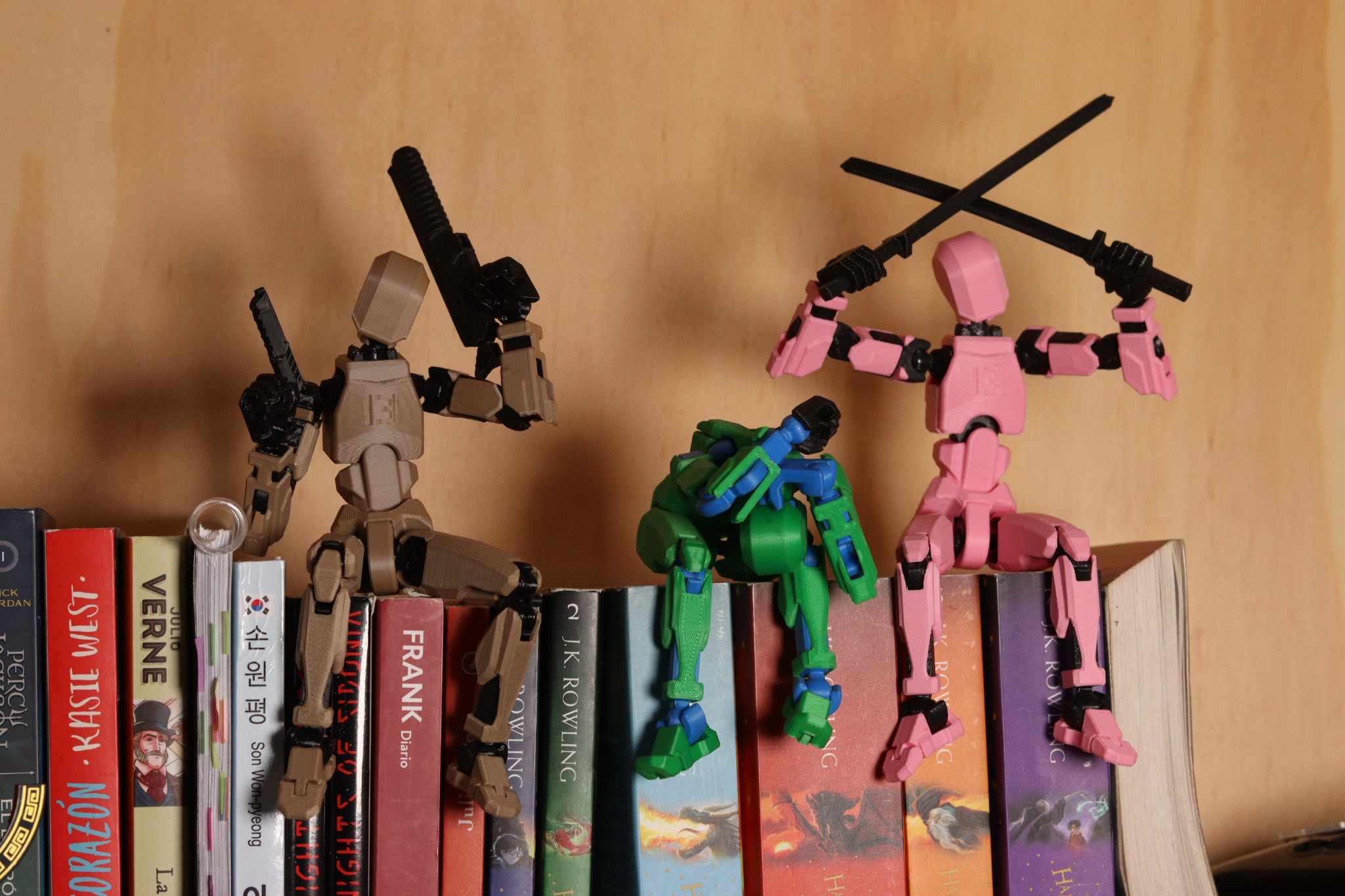 Tres robots articulados, marrón, verde y rosa, sobre una biblioteca